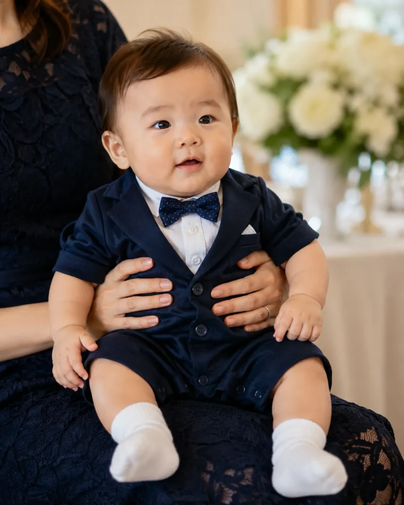 結婚式の赤ちゃんの服装例。ネイビーのタキシード風ロンパースに蝶ネクタイ、白の靴下