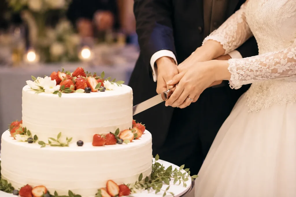 ケーキ入刀の場面。新郎新婦が一緒にナイフを持ち、いちごを飾った2段の生ケーキに入刀している